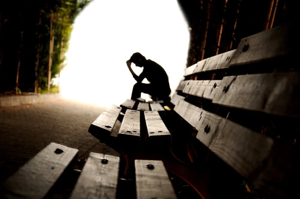 man sitting outside with hand on head, needing help for homelessness and addiction