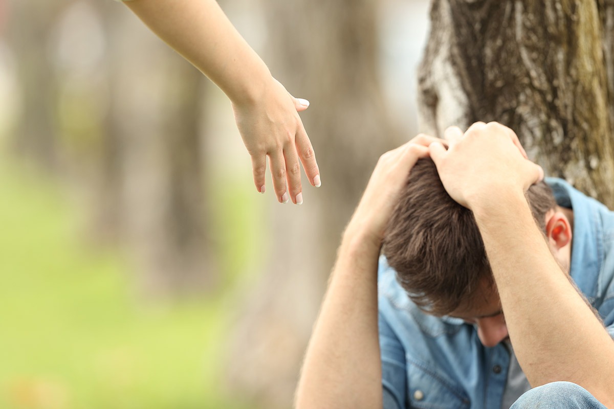 hand reaching out to sad individual showing how to help an addict
